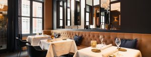 Restaurantzaal met gecapitonneerde bank, witte tafellinnen en donkere wandbetimmering.