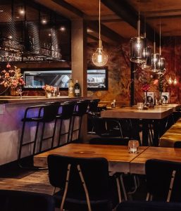 Warm restaurantinterieur met bar, tafels en hanglampen.