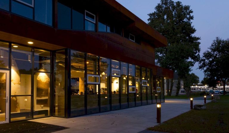 Restaurantgevel met grote ramen in de avond.