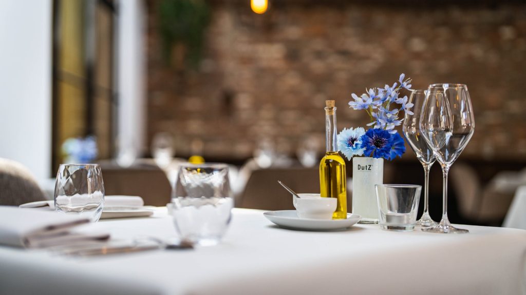 Close-up van gedekte restauranttafel met bloemen, glazen en tafellinnen.