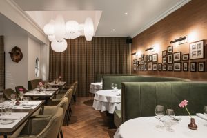 Restaurantzaal met zachtgroene bank en witte tafelkleden.