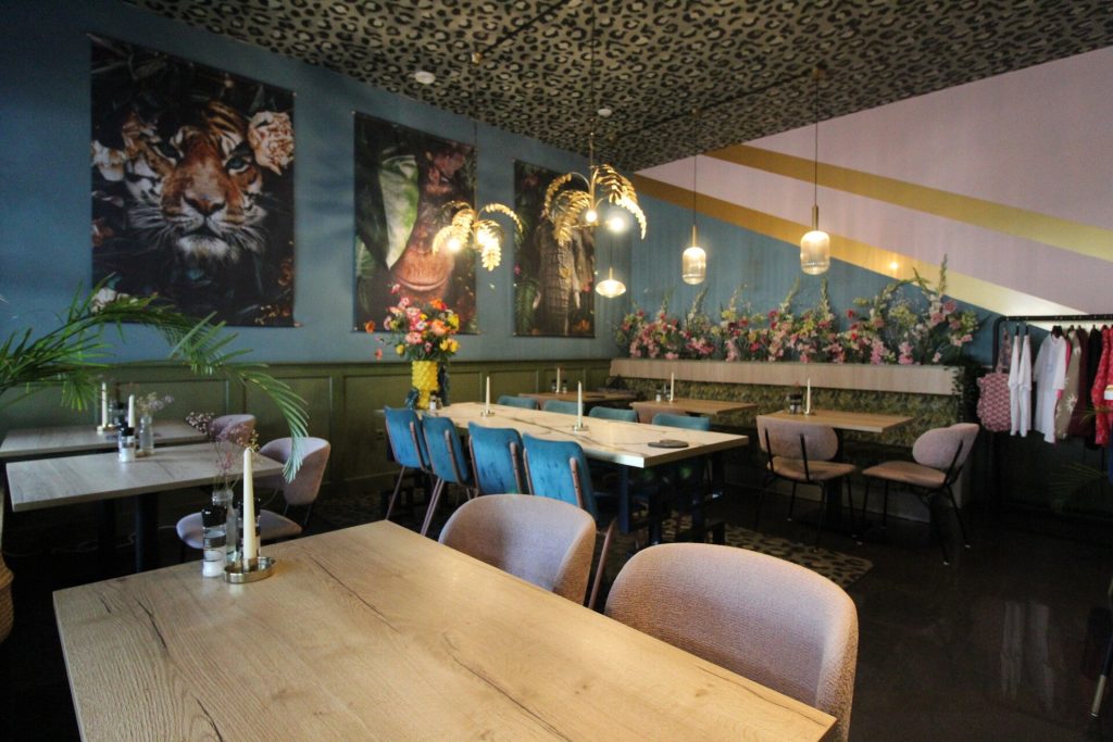 Restaurantzaal met houten tafels, zitbanken en kleurrijke wandkunst.