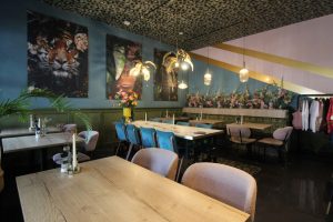 Restaurantzaal met houten tafels, zitbanken en kleurrijke wandkunst.