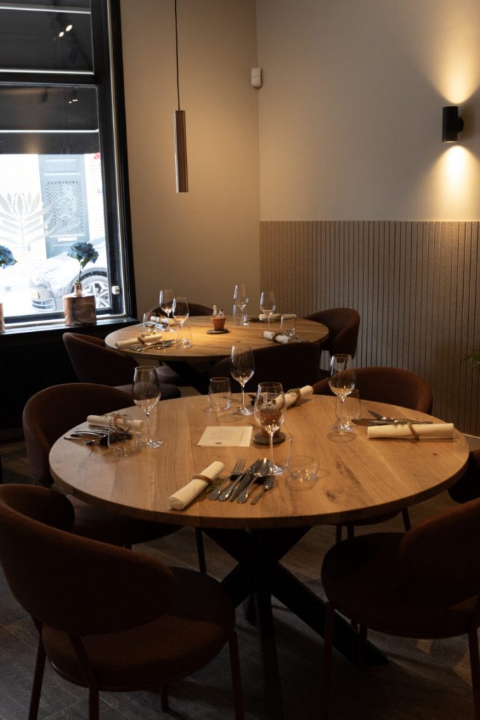 Gedekte ronde tafels in een warm verlicht restaurantinterieur.