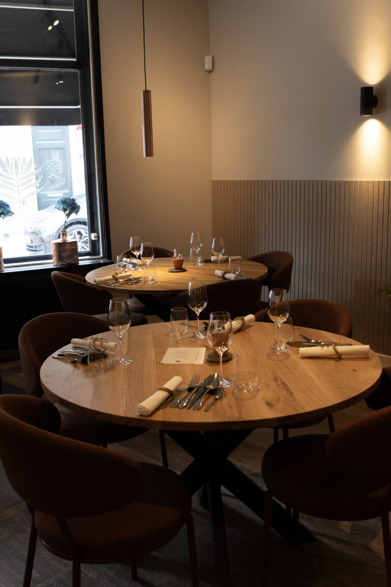 Gedekte ronde tafels in een warm verlicht restaurantinterieur.