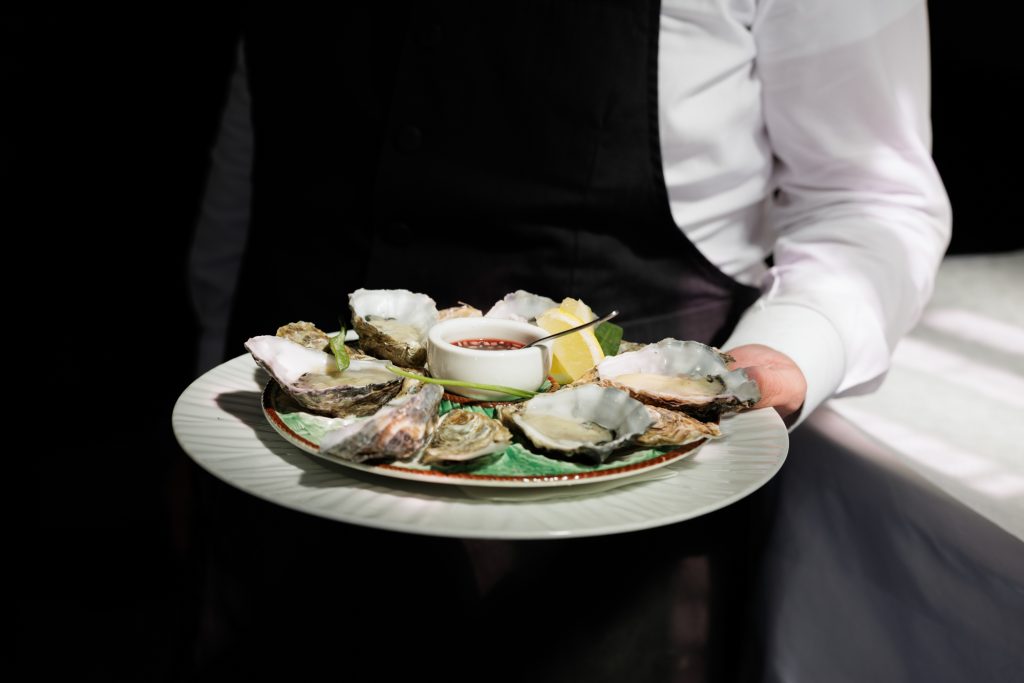 Een medewerker presenteert een schaal oesters tegen een donkere achtergrond.