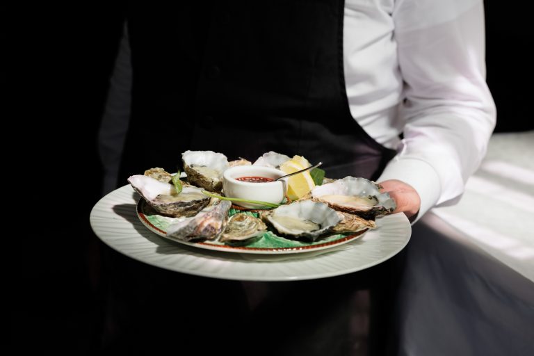 Een medewerker presenteert een schaal oesters tegen een donkere achtergrond.
