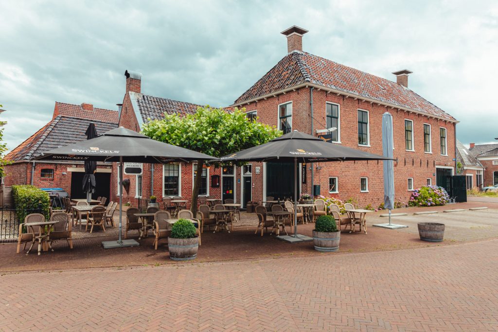 Gevel van de herberg met ruim terras en parasols.
