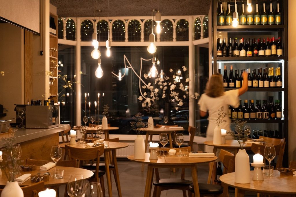 Knusse eetzaal met houten tafels, wijnkasten en hanglampen.