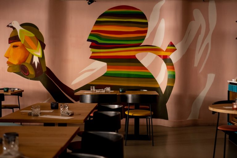 Restaurantzaal met tafels en een kleurrijke abstracte muurschildering.