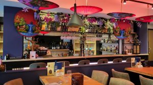 Kleurrijk interieur met bar, decoratieve parasols en eettafels.