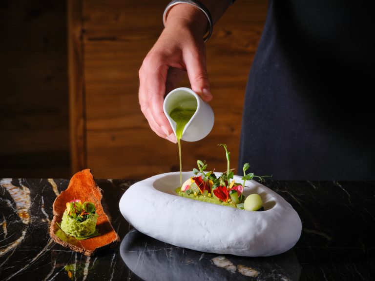 Verfijnd kleurrijk gerecht in een witte schaal terwijl saus wordt ingeschonken.