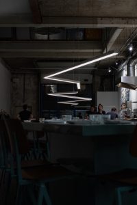 Donker restaurantinterieur met betonnen plafond en geometrische verlichting.
