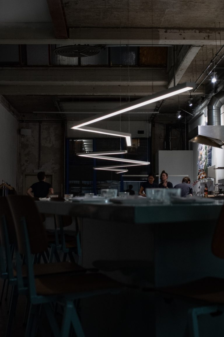 Donker restaurantinterieur met betonnen plafond en geometrische verlichting.