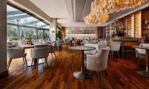 Lichte restaurantzaal met bar, brede ramen en goudkleurige verlichting.