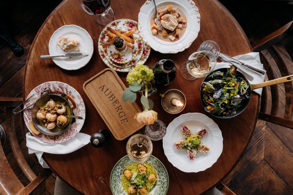 Meerdere bistrogerechten, brood en wijnglazen van boven op een ronde houten tafel.