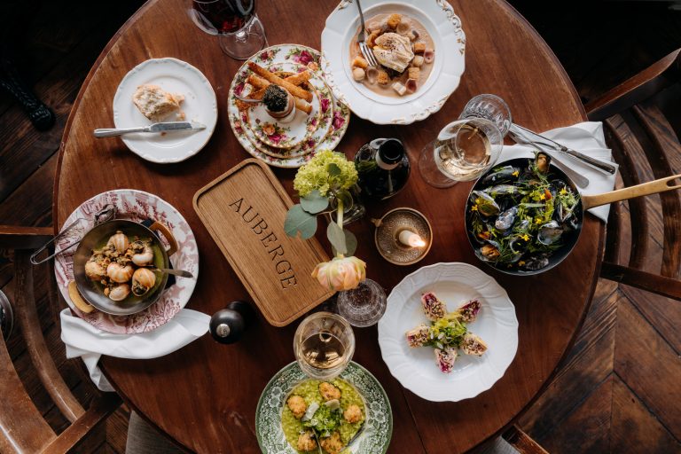 Meerdere bistrogerechten, brood en wijnglazen van boven op een ronde houten tafel.