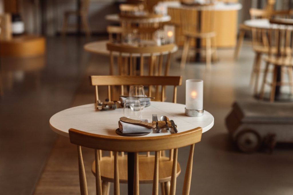 Gedekte ronde tafel en houten stoelen in een warme caféruimte.