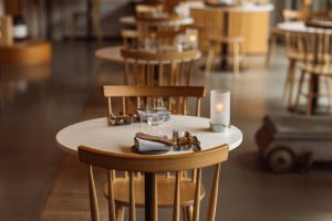 Gedekte ronde tafel en houten stoelen in een warme caféruimte.