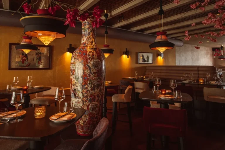 Warm restaurantinterieur met gedekte tafels en grote gedecoreerde vaas.