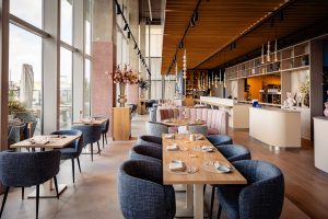 Lichte restaurantzaal met roze en blauwe stoelen.