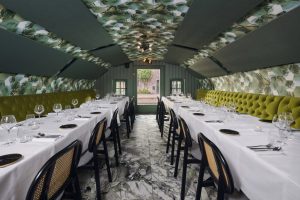 Gedekte lange tafels in een groene zaal met bloemenplafond.
