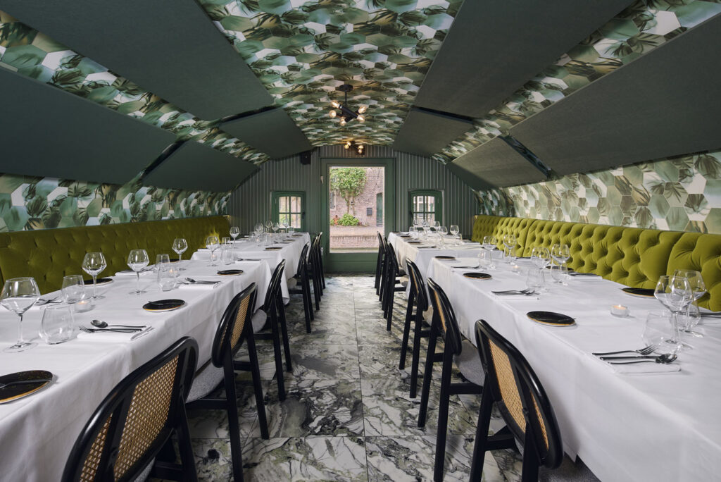 Gedekte lange tafels in een groene zaal met bloemenplafond.