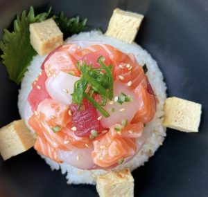 Rond opgemaakt visgerecht met garnering op een donker bord.