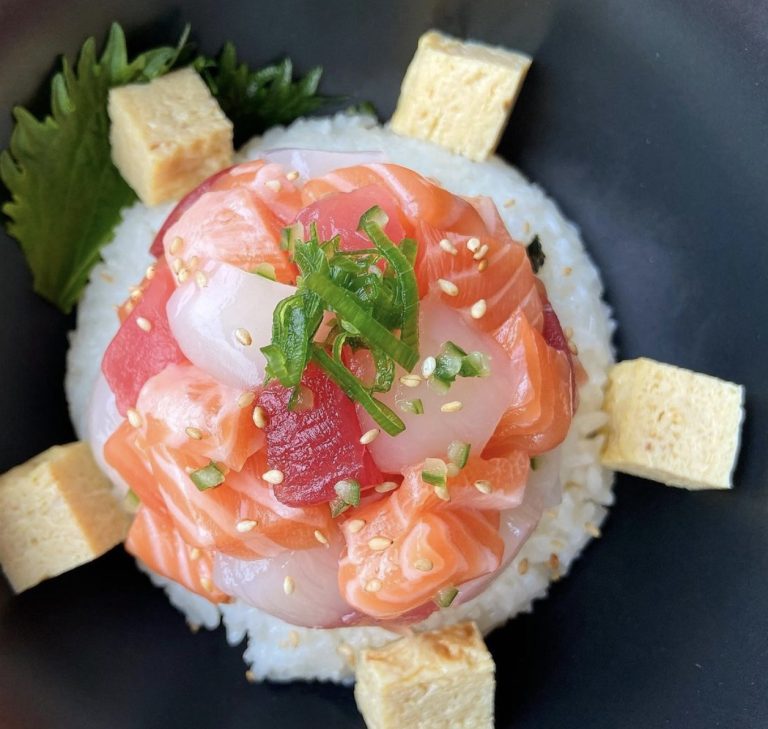 Rond opgemaakt visgerecht met garnering op een donker bord.