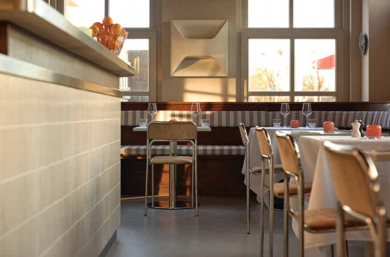 Lichte eetzaal met bar, banken en gedekte tafels.