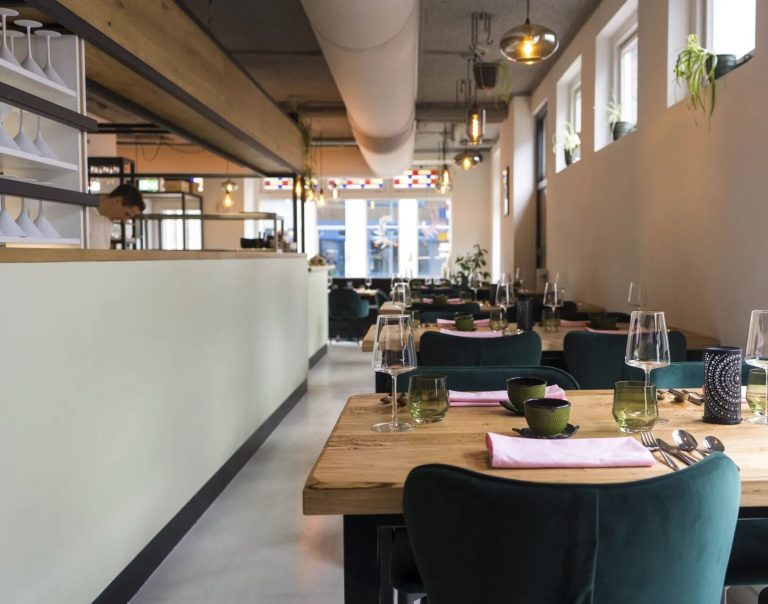 Lichte langgerekte eetzaal met gedekte tafels en groene stoelen.