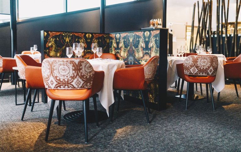 Kleurrijke stoelen en gedekte tafels in restaurantzaal.