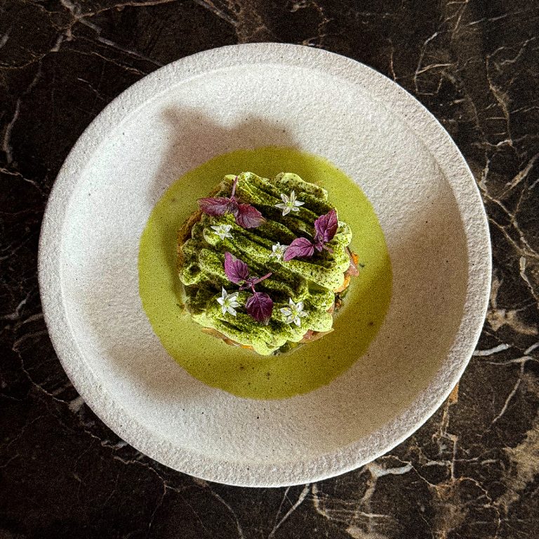 Groen gerecht met bloemen in rond wit bord.
