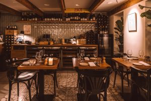 Intieme eetzaal met houten balken, bar en gedekte houten tafels.