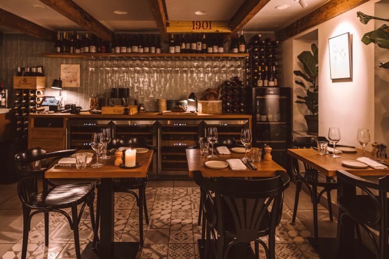 Intieme eetzaal met houten balken, bar en gedekte houten tafels.