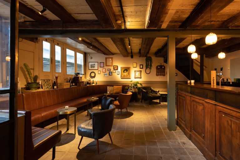 Warm interieur met houten balken, zitbanken en wandkunst.