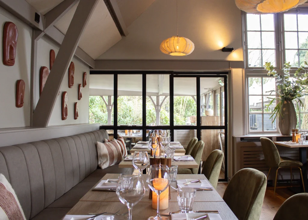 Lichte brasserie met gedekte tafels, wandbank en grote ramen.