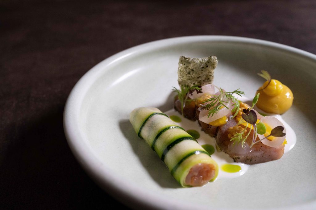 Verfijnd gerecht met groene groenterolletjes op een wit bord.