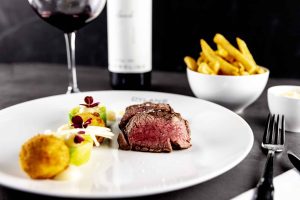 Steakgerecht met garnituren, frites en wijn.