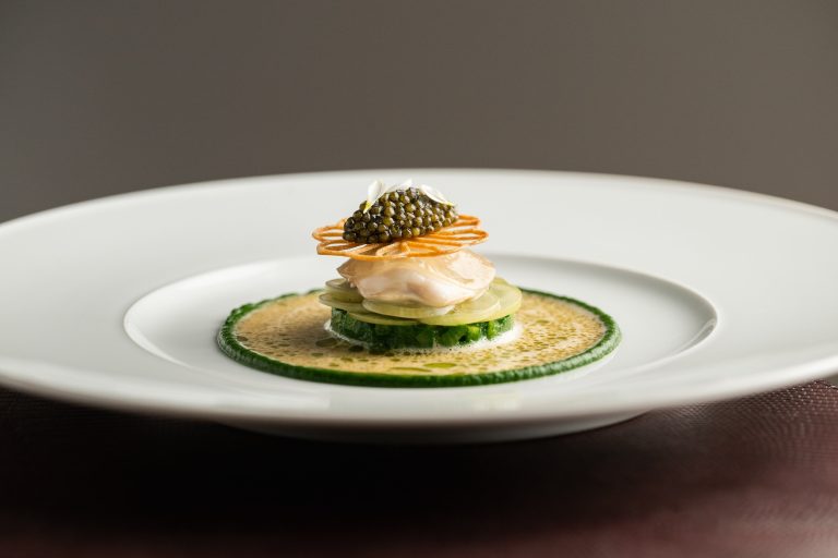 Fijn opgebouwd gerecht in groene saus op een groot wit bord.