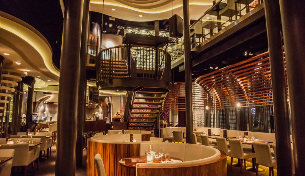 Ruim restaurantinterieur met centrale trap en warm licht.