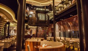Ruim restaurantinterieur met centrale trap en warm licht.