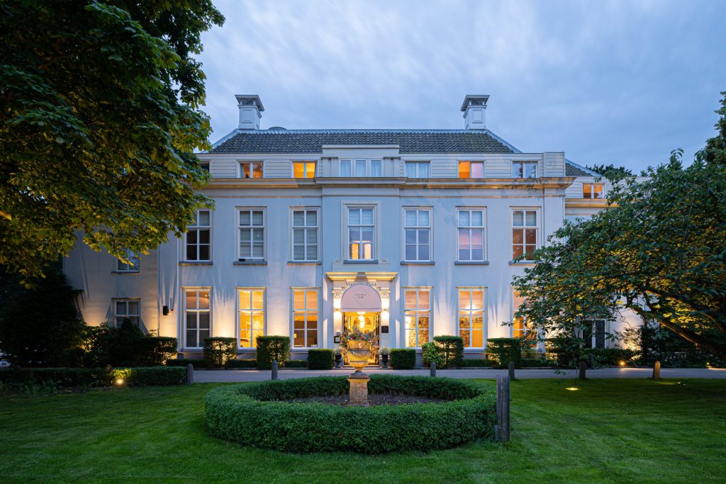 Verlichte witte villa en voortuin in avondlicht.