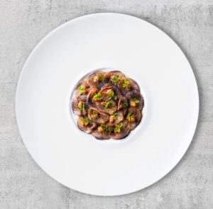 Modern opgemaakt gerecht centraal op wit bord.