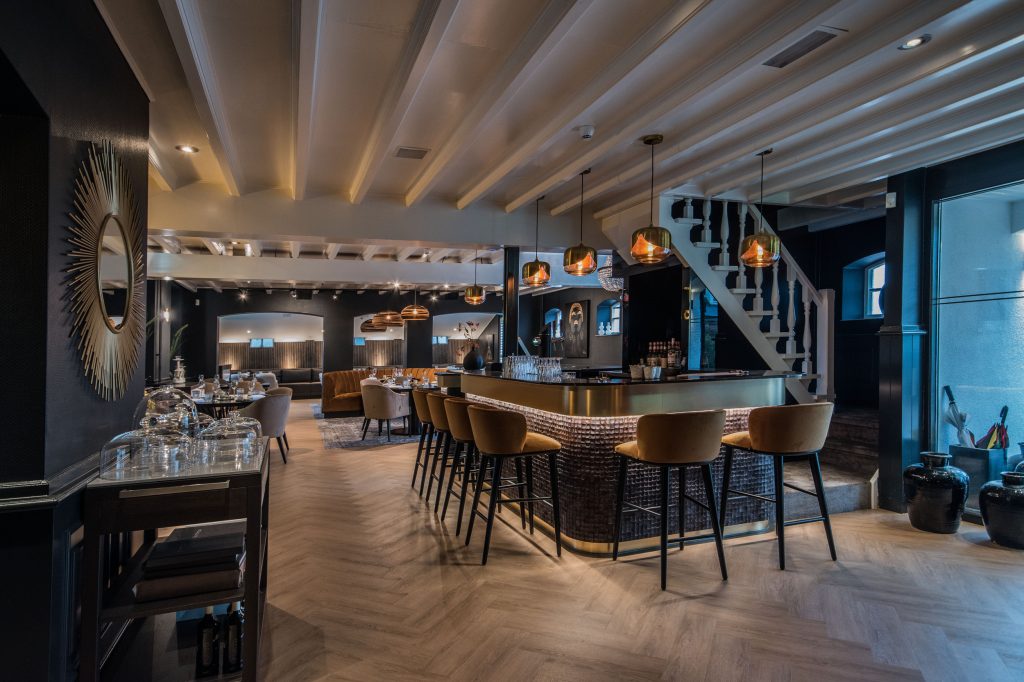 Eetzaal met ronde bar, barkrukken en gedekte tafels.