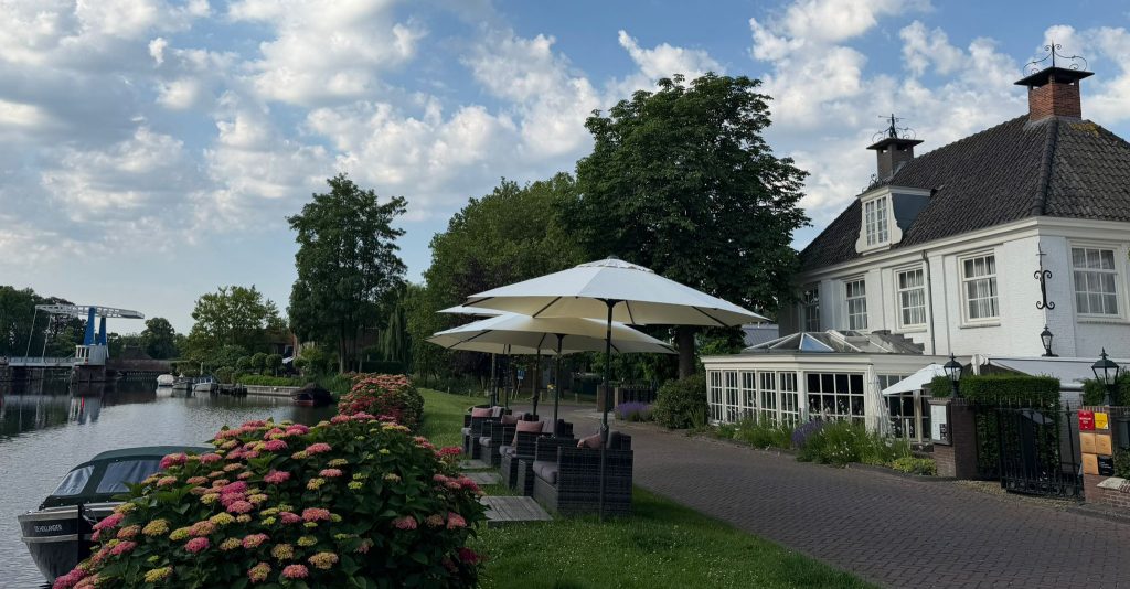 Restaurant aan het water met witte parasol en tuin.