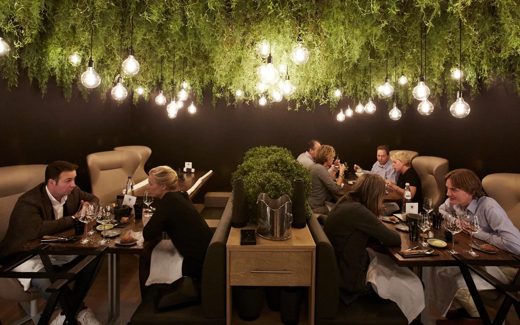 Restaurantzaal met gasten onder groen plafond en veel hanglampen.