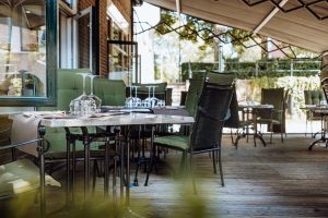 Gedekte tafels op het overdekte restaurantterras bij groene kozijnen.