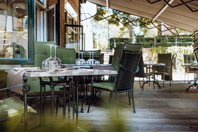 Gedekte tafels op het overdekte restaurantterras bij groene kozijnen.