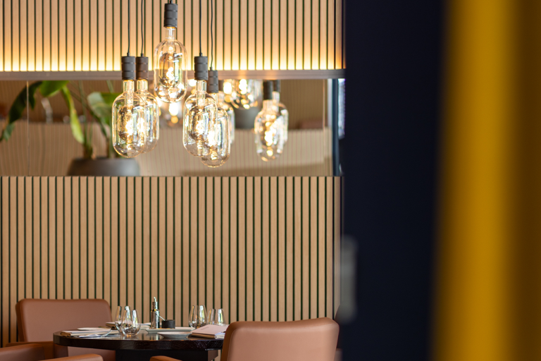 Restauranttafel met kroonluchter en verticale houten wandbekleding.